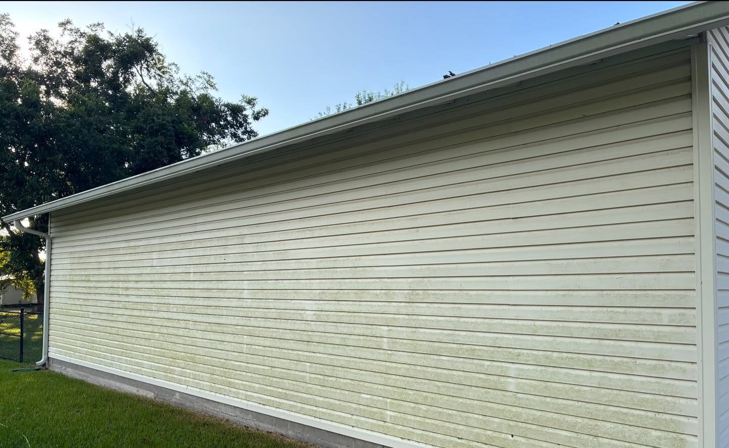 The gable end of a house, the cream vinyl siding streaked green and grey with algae before washing