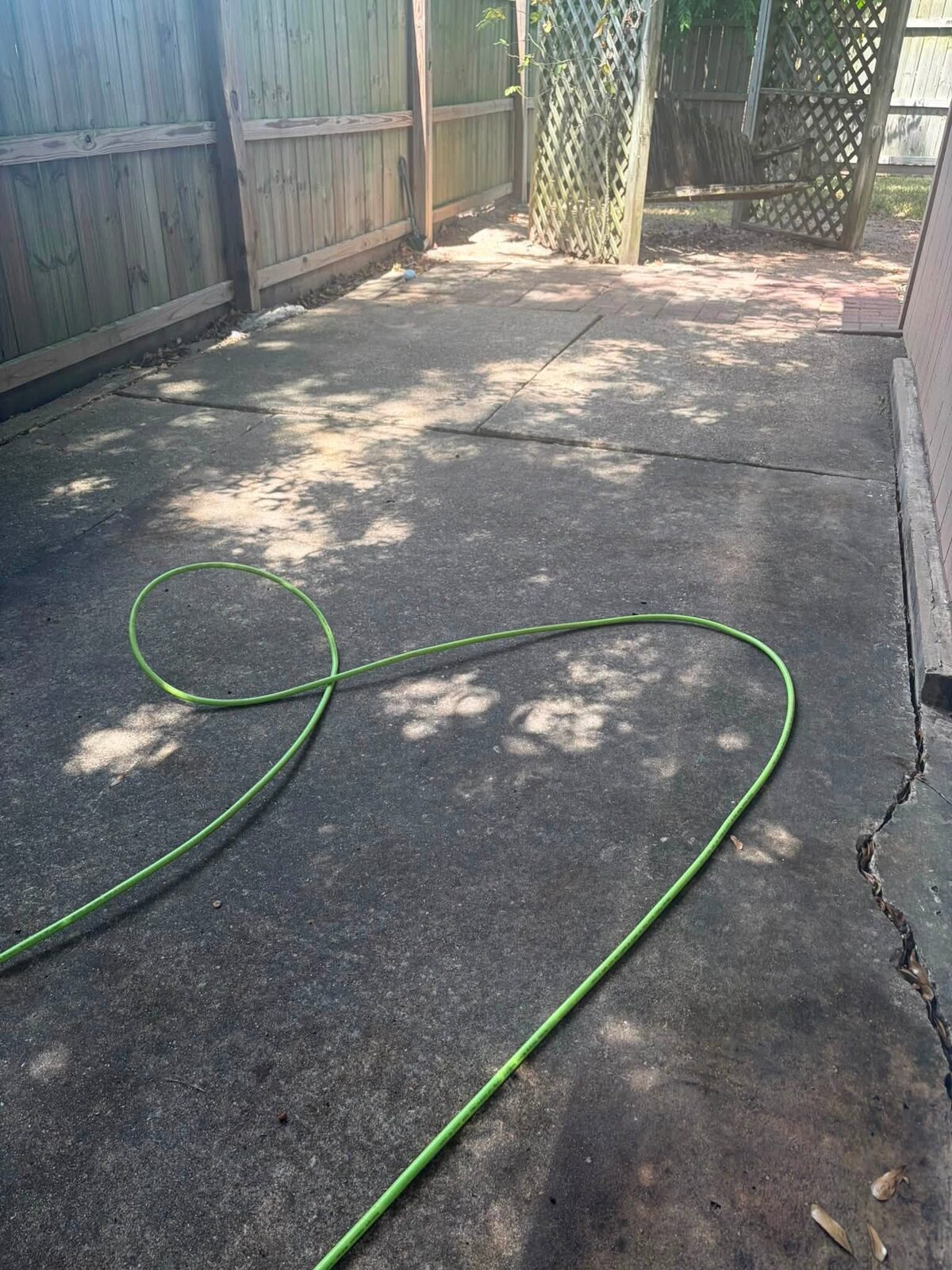 A shaded back patio slab darkened grey with dirt, a hose coiled across it