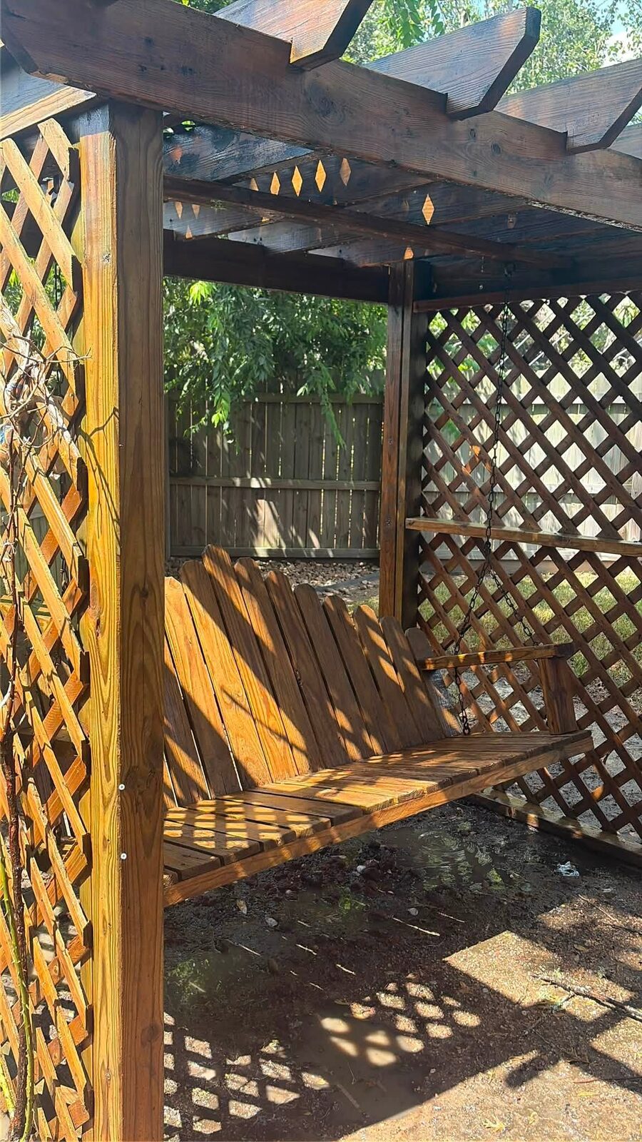 The same pergola and swing washed back to warm golden timber, the grain showing again