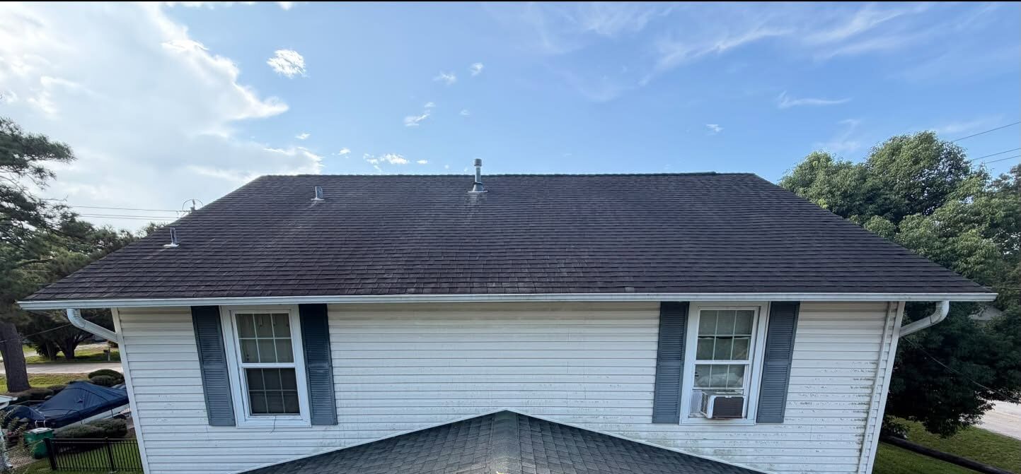 A white house with dark roof shingles seen from above, the siding dull and streaked before washing