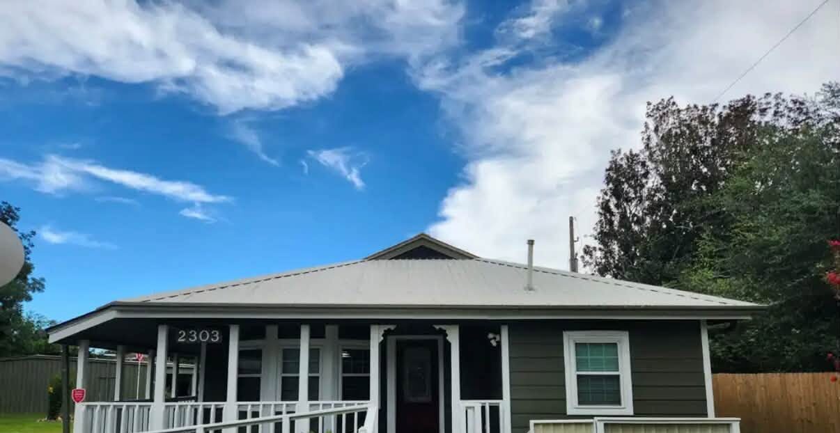 The same cottage after cleaning, the metal roof pale and even and the porch bright white